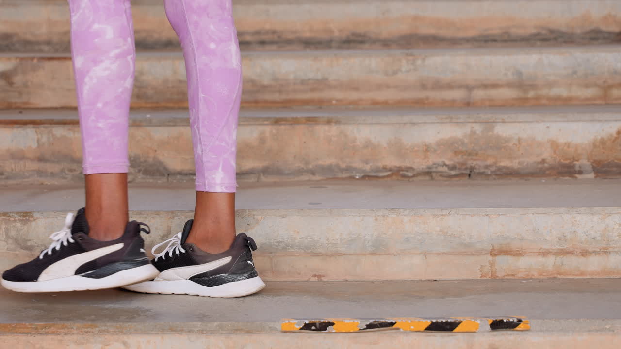 Gambe su scale di cemento che indossano leggings viola, primo piano di scarpe da ginnastica nere e passo fermo; un jogger fitness urbano che scende le scale della città, con contatto della suola e cadenza ritmica, energia da allenamento e stile casual.