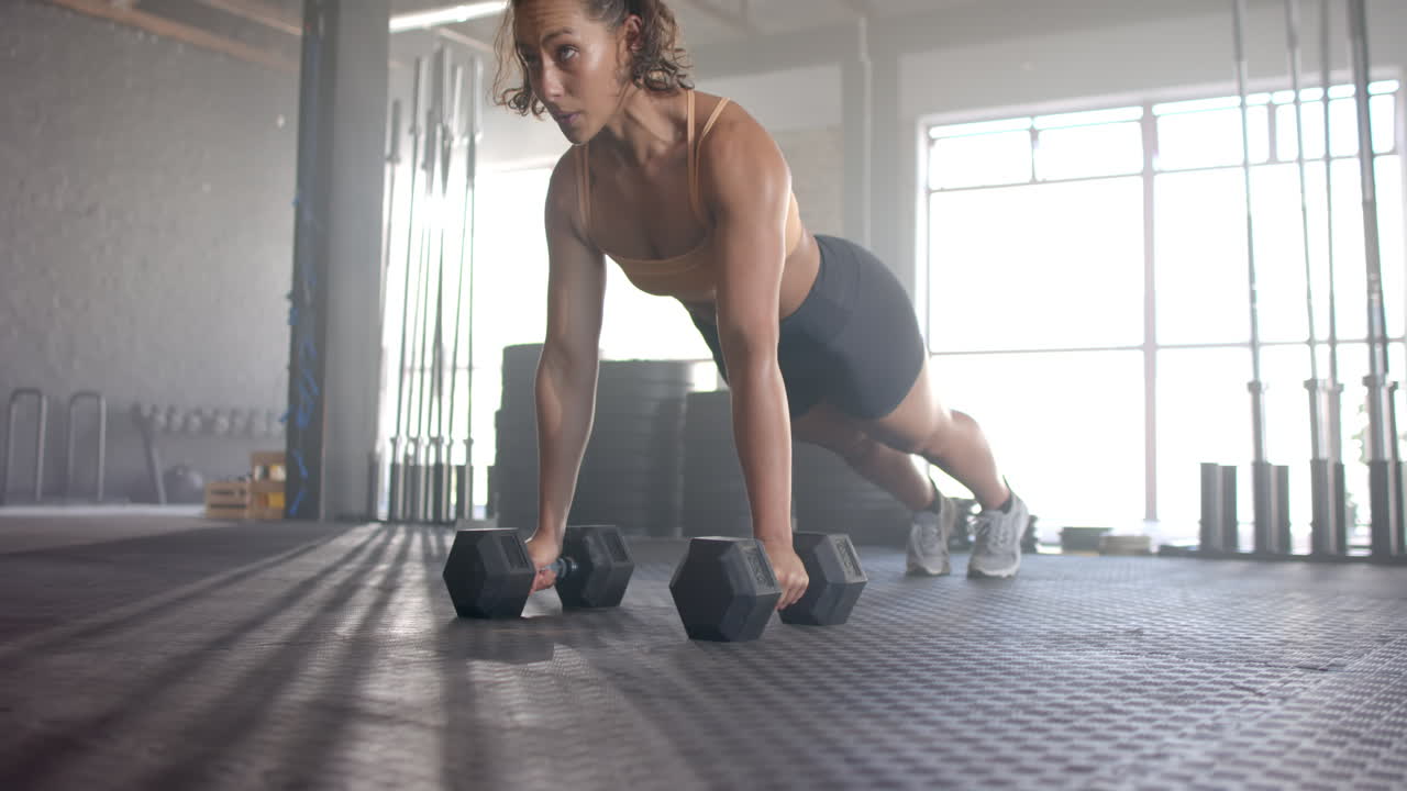 Doing push-ups with dumbbells, woman exercising in gym, building strength
