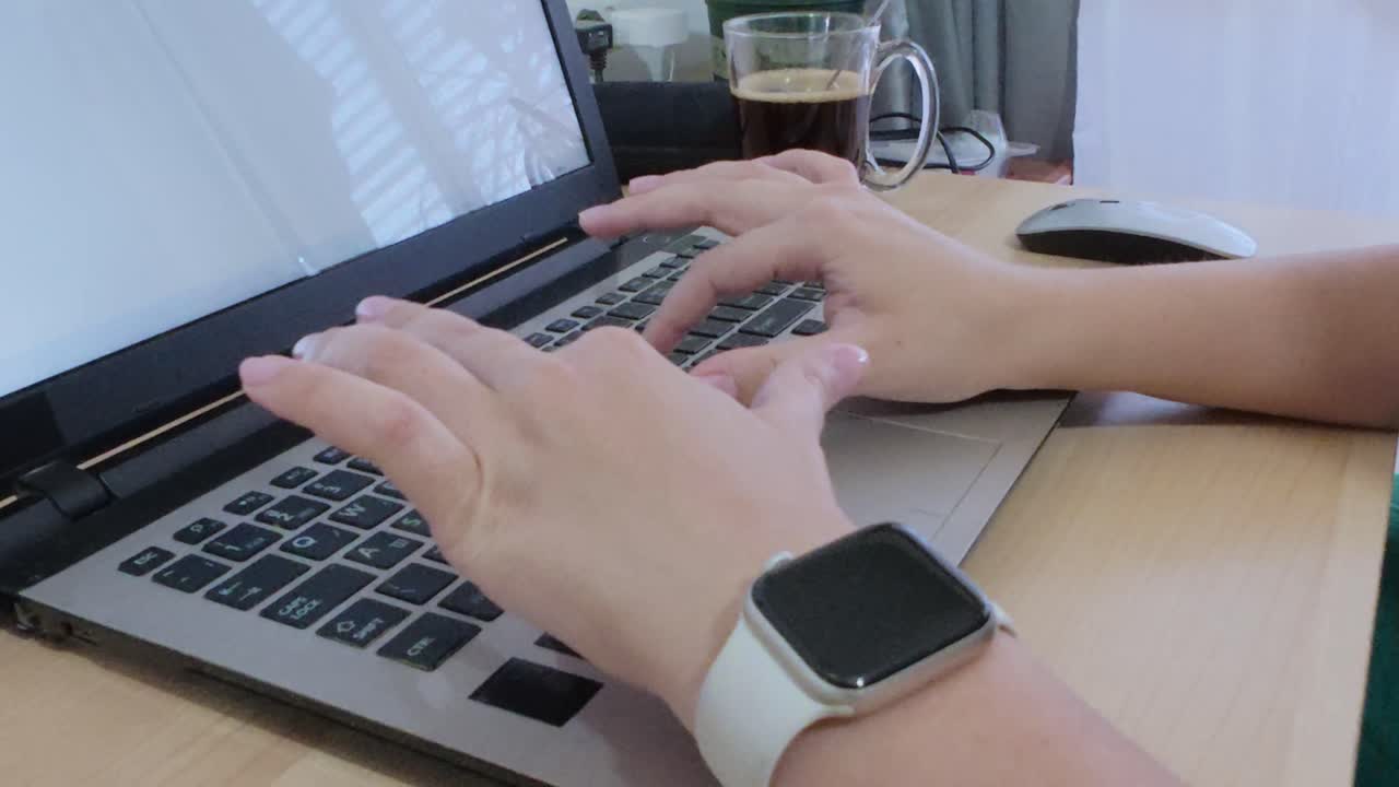 Close-up of hands actively typing on a laptop keyboard, with coffee and smartwatch nearby.