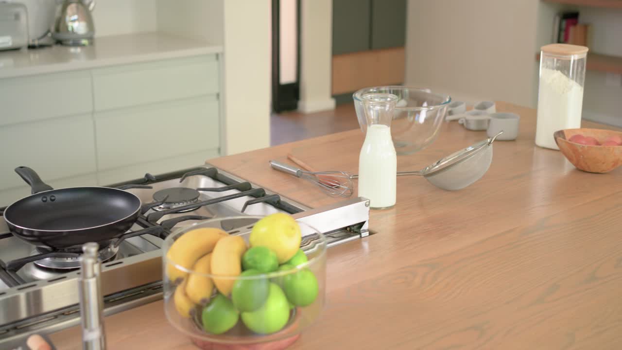 Telecamera che si muove sul bancone della cucina, rivelando una padella, un barattolo di farina e ciotole per la preparazione.