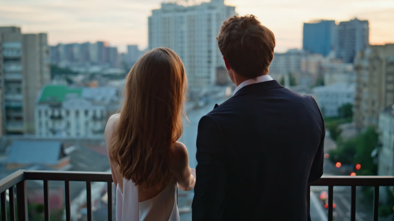 Elegant couple standing balcony overlooking evening city. Young man and woman