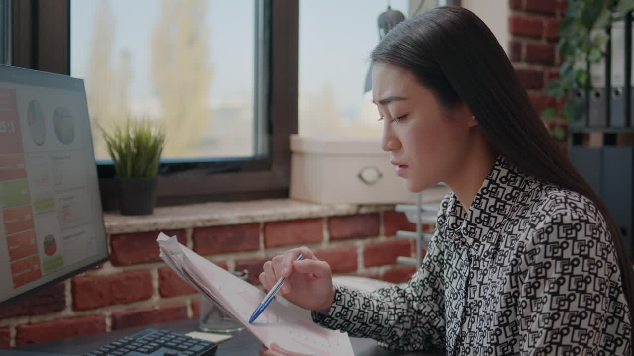 Asian woman comparing charts on papers and computer