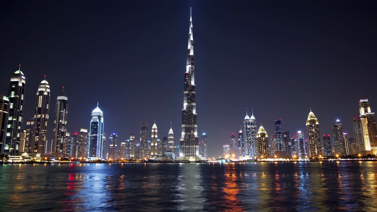Illuminated Burj Khalifa towering over the Dubai skyline at night, casting reflections in the serene waters below, creates a captivating urban landscape filled with vibrant city lights