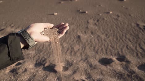 male hand dropping releasing sand on the desert