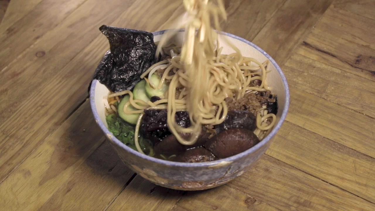 Bacchette che mescolano i condimenti in una ciotola di ramen fatto a mano