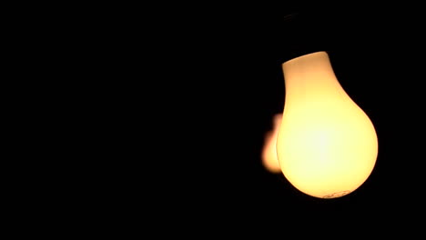 three bare illuminated light bulbs swing against a black background