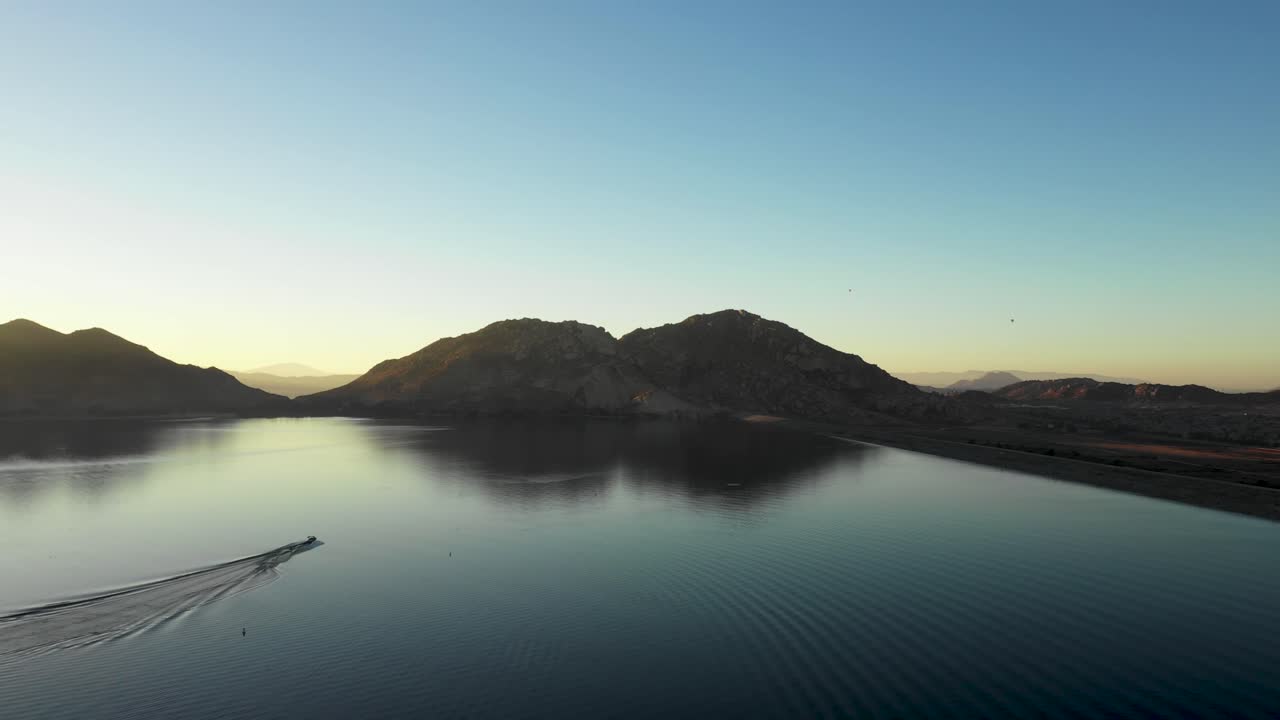 스키 보트와 스키 선수가 떨어질 때까지 호수와 같은 유리를 가로질러 스키를 고 있습니다.