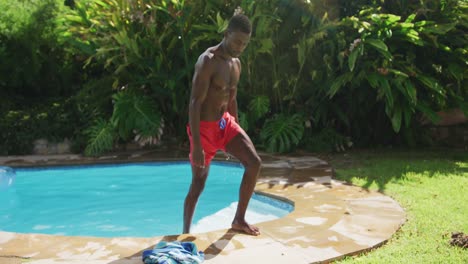 handsome african american man walking out of in swimming pool in sunny garden
