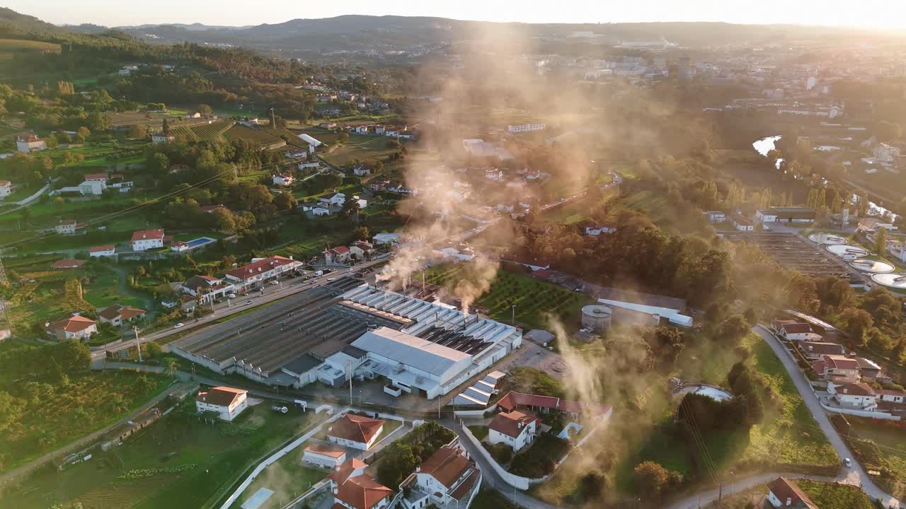 industrial factory releasing smoke over a rural area during sunset - aerial