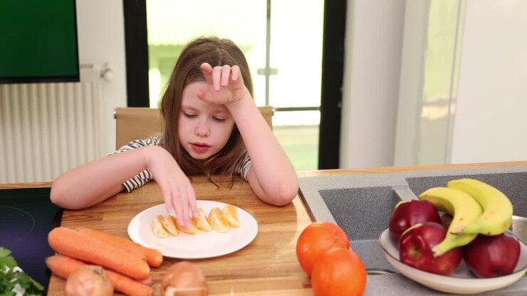 A girl sitting at a table with fruit and vegetables