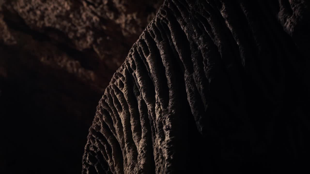 Primo piano di una formazione di grotta calcarea a Ibiza che mostra una superficie di stalattite texturizzata, illuminata da una debole luce naturale che crea ombre drammatiche