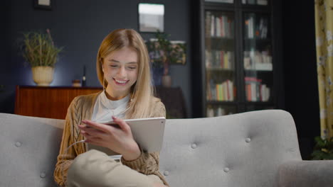 Lächelnde-Junge-Frau-Mit-Kopfhörern-Mit-Tablet,-Während-Sie-Zu-Hause-Auf-Der-Couch-Sitzt-1