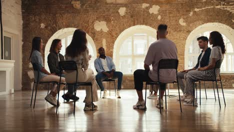 Group-therapy-meeting-for-adults-in-a-brick-room.-Participants-in-group-therapy-sit-in-a-circle-and-communicate