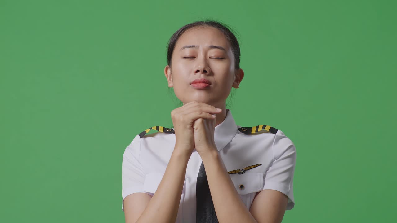緑色の画面の背景のスタジオに立っている間何かのために祈っているアジアの女性パイロットのクローズアップ