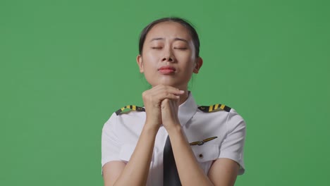 close up of asian woman pilot praying for something while standing in the green screen background studio