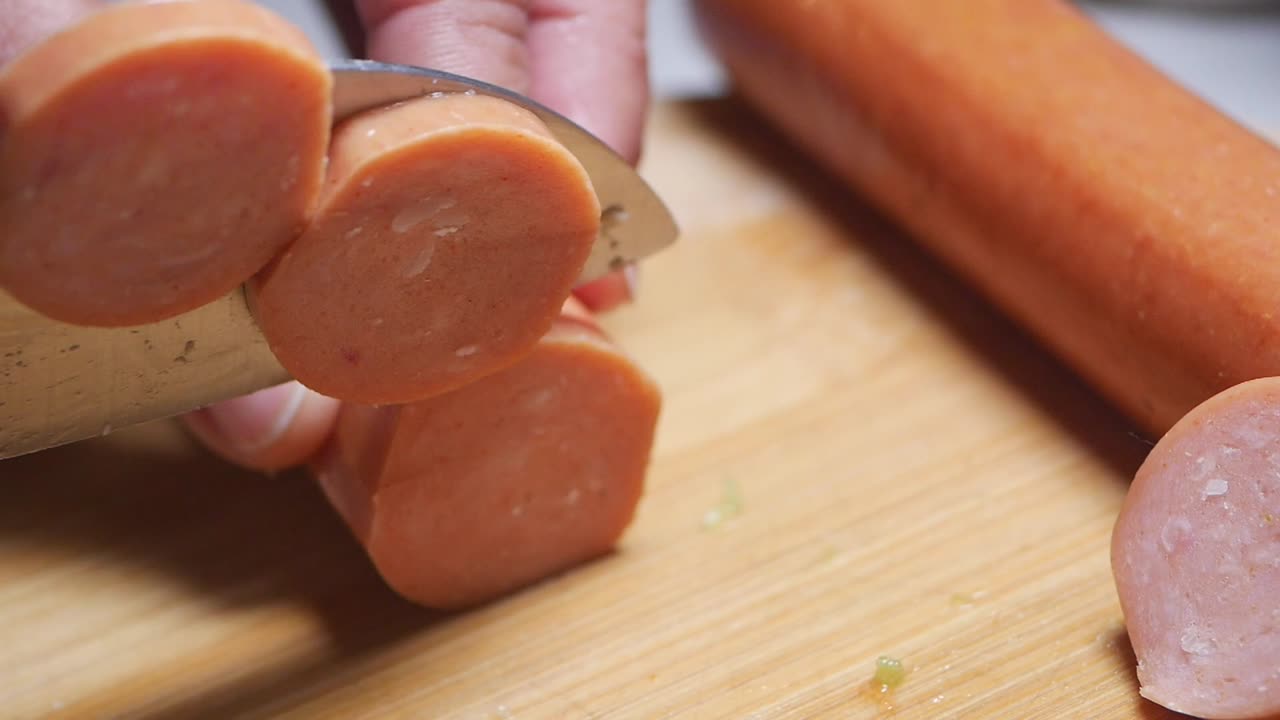 Primo piano di una mano che taglia una salsiccia su un tagliere di legno