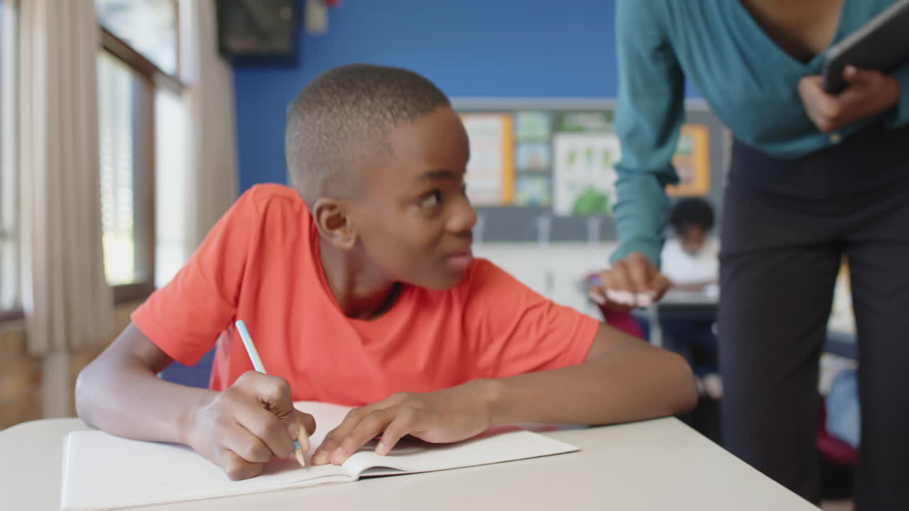 In school, boy writing in notebook and smiling while talking to teacher