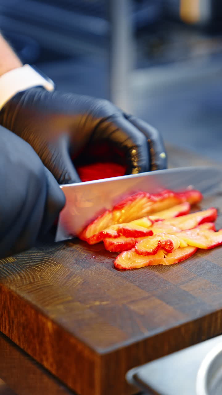 Unrecognized cook's hands in black gloves slice fish with a big knife. Preparing seafood. Close up. Vertical video.