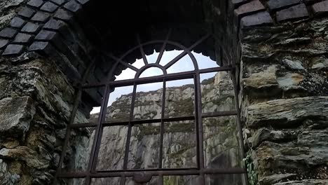 Ornate-wrought-iron-arched-window-frame-remains-in-Welsh-quarry-brickwork-factory-ruins,-Anglesey