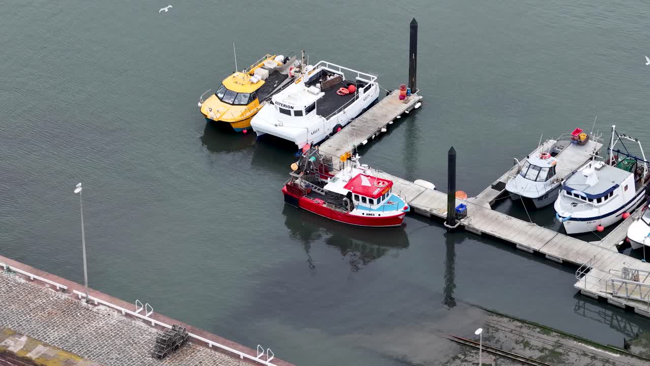Aerial shot of fishing boats moored at marina dock, overcast daylight, gentle camera movement