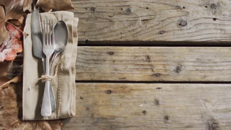 close up view of cutlery set over a napkin and autumn leaves with copy space on wooden surface