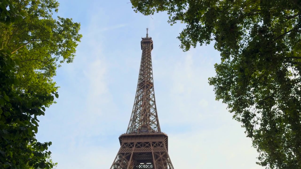Icónica Torre Eiffel dominando el horizonte parisino, enmarcada por exuberantes árboles verdes en un claro día de verano, un monumento famoso