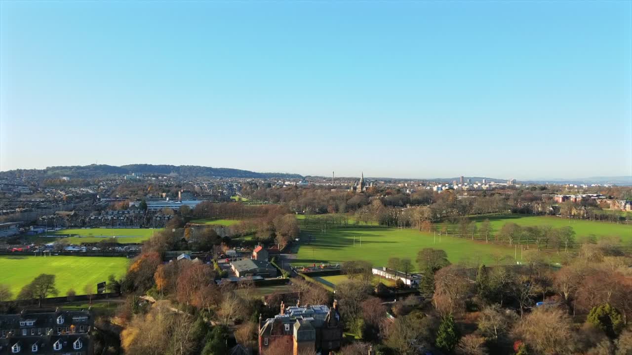 Riprese aeree del Fettes College, un edificio iconico che ricorda una torre di chiesa, circondato da lussureggianti campi verdi e aree residenziali a Edimburgo, Scozia, catturate sotto un cielo azzurro limpido