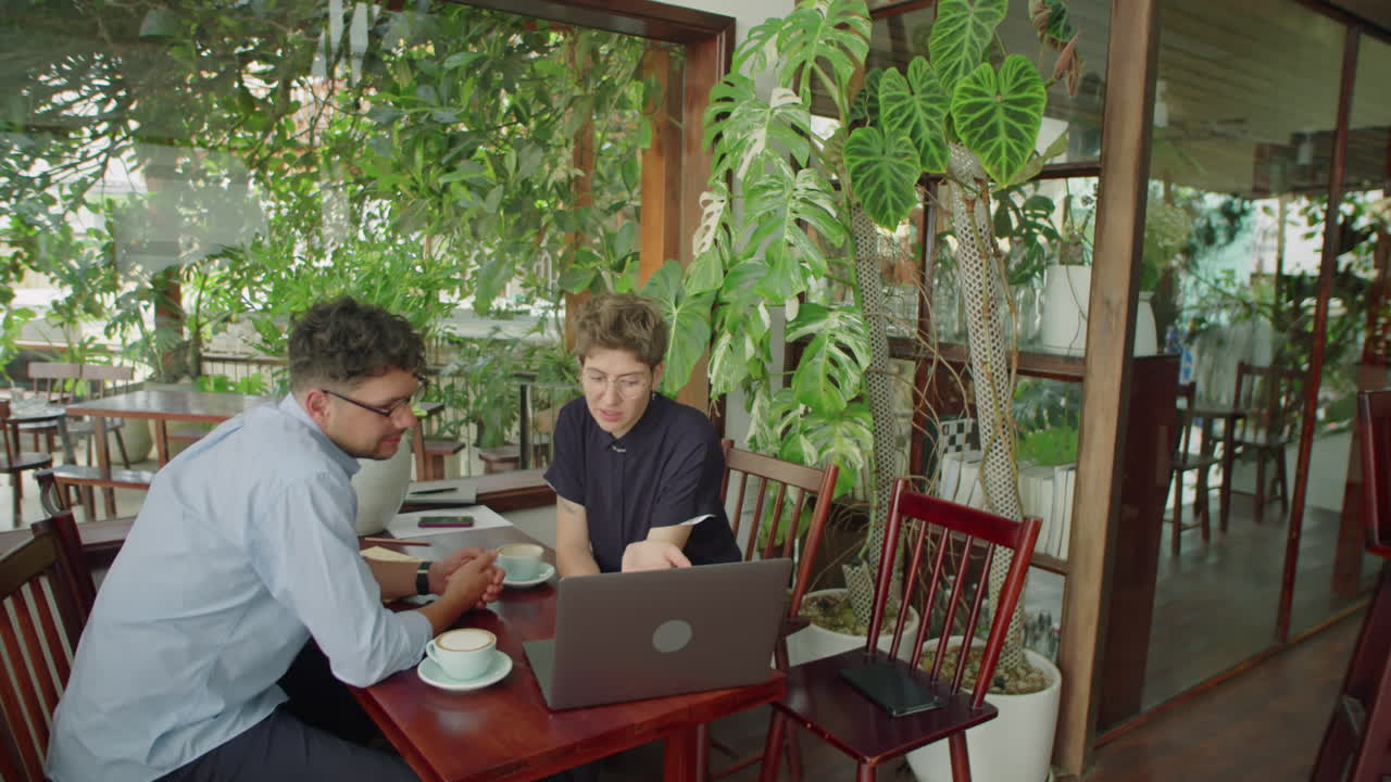 Colleagues Working on Laptop and Speaking in Outdoor Cafe