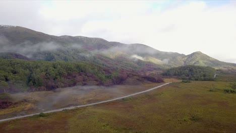 Aerial-flight-over-foggy-mountains-and-grassland-following-road-in-Tasmania-in-Australia,-full-shot-moving-forward-with-clouds-in-background