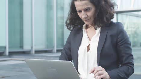 focused businesswoman using laptop outside, looking at display, getting good news, making winners gestures