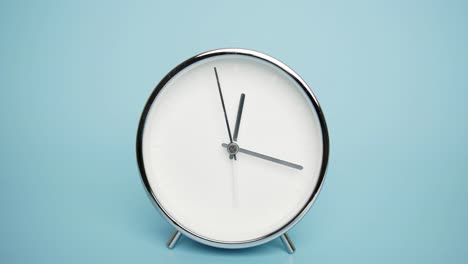 silver alarm clock isolated on a blue background, time starts walking at 12 o'clock.