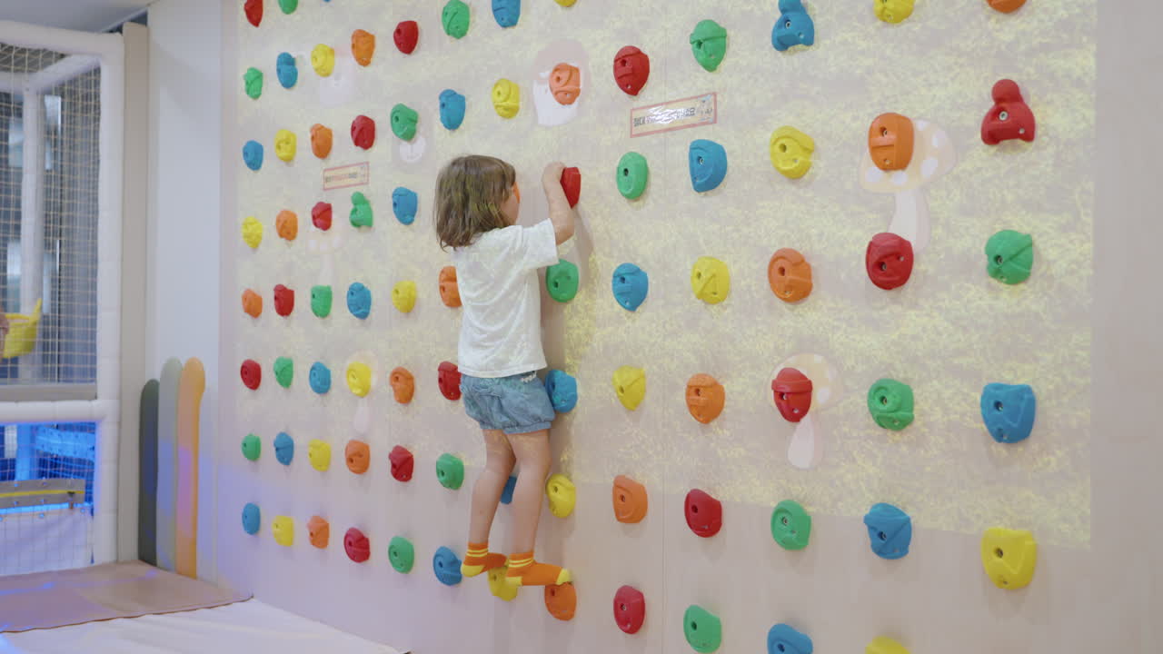 una niña juguetona se sube usando garras en la pared de escalada dentro de la sala de juegos - disparo de mano