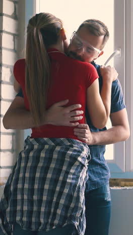 young woman with ponytail hugs handsome husband applying spray foam insulation on windowsill in light room