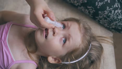 woman-gives-eye-drops-to-little-girl-lying-on-soft-bed