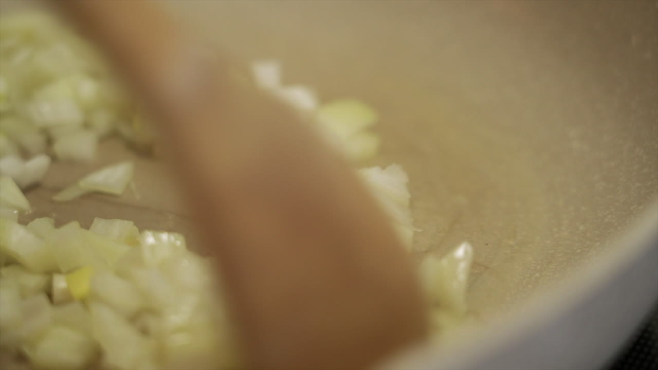 Chef using a wooden spoon to sautee some sweet white onions