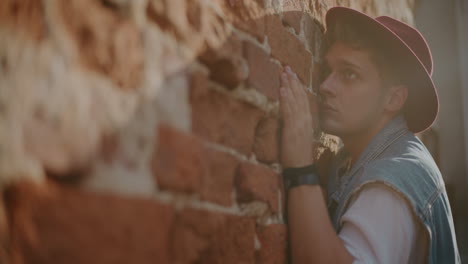 hombre apoyado en una pared de ladrillo