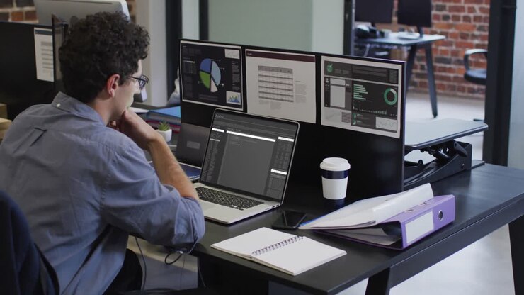 Caucasian man sitting at desk watching coding data processing on laptop and computer screen