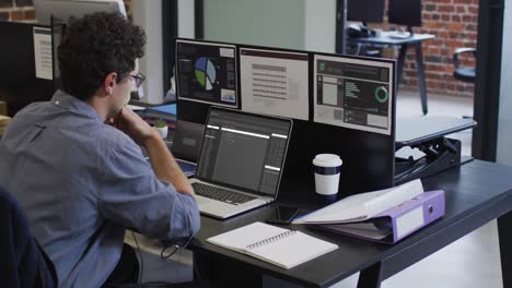 hombre caucásico sentado en el escritorio viendo el procesamiento de datos de codificación en la computadora portátil y la pantalla