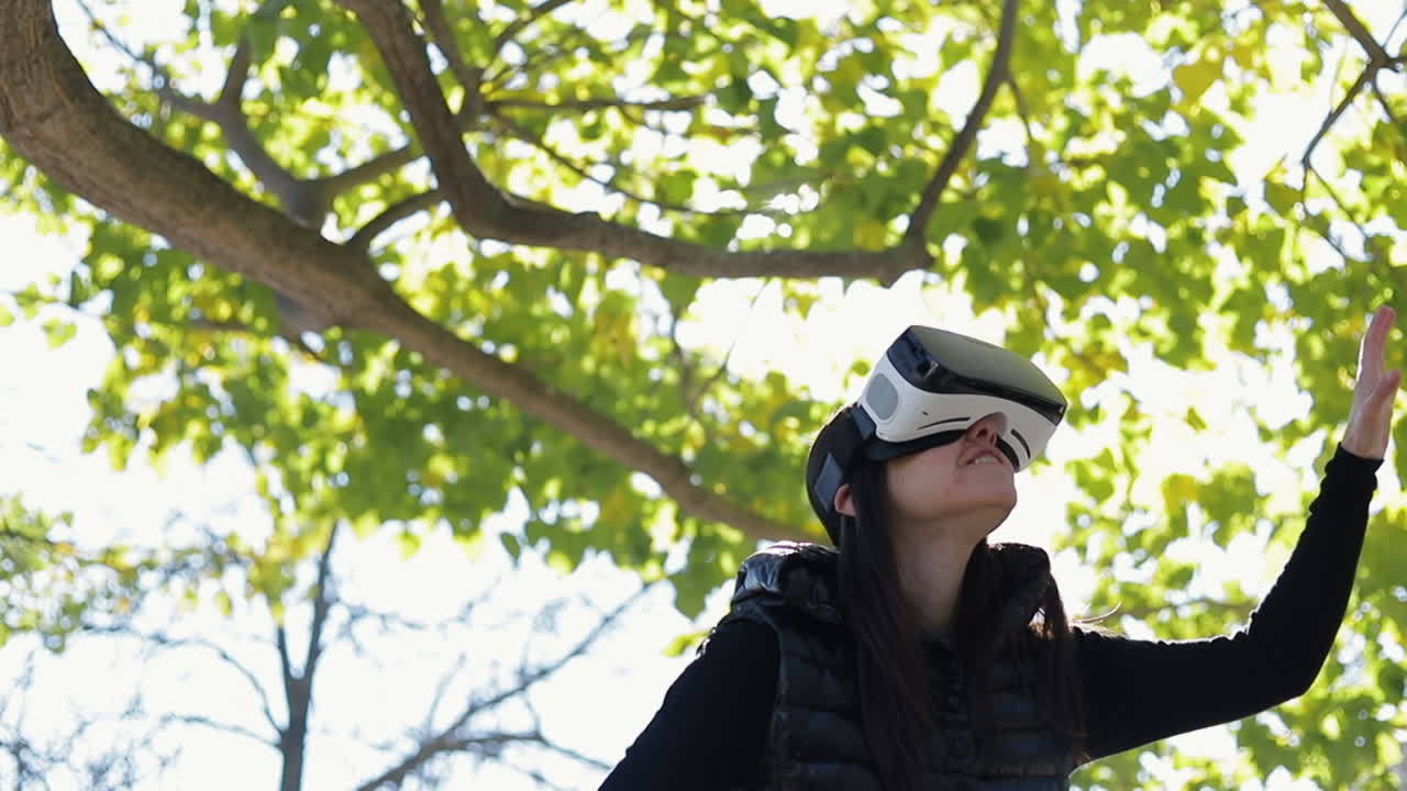 joven de cabello oscuro en un cálido chaleco negro caminando en el parque de otoño temprano