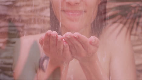 animation of palm leaves over happy biracial woman splashing face in shower