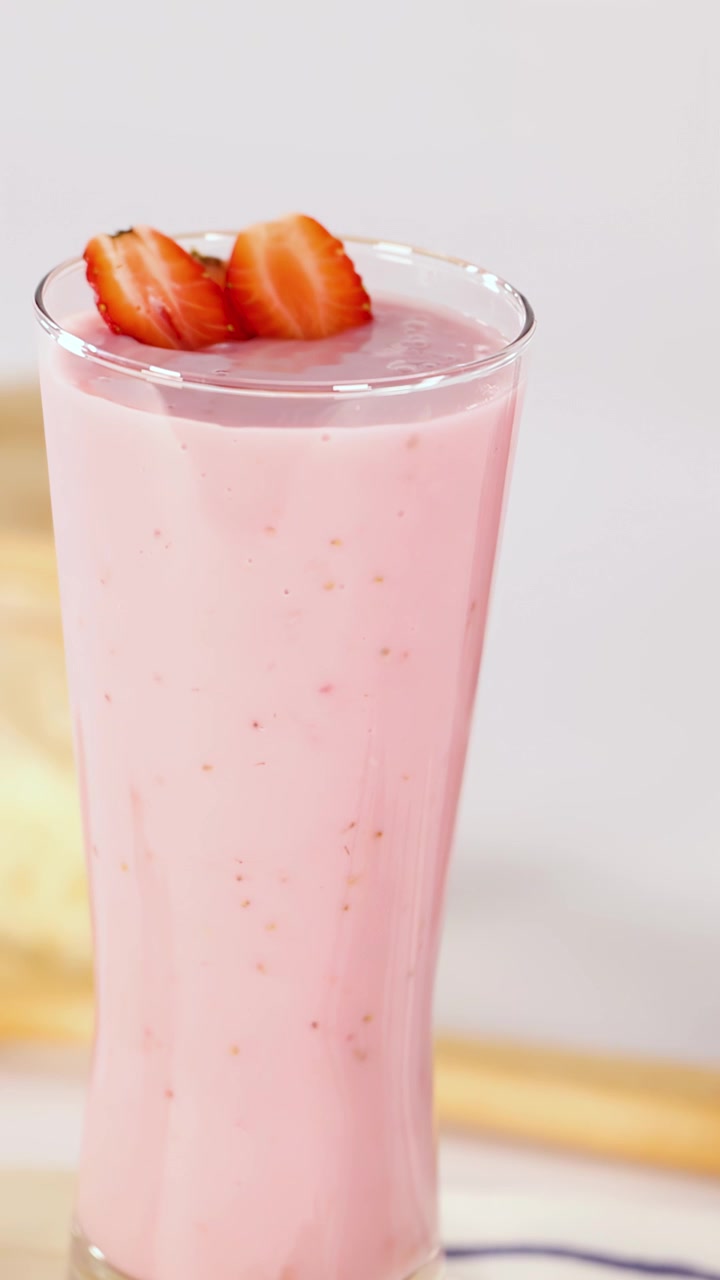 Batido de fresa rosa vertido en vaso, adornado con fresas en rodajas, iluminación suave y brillante, movimiento mínimo