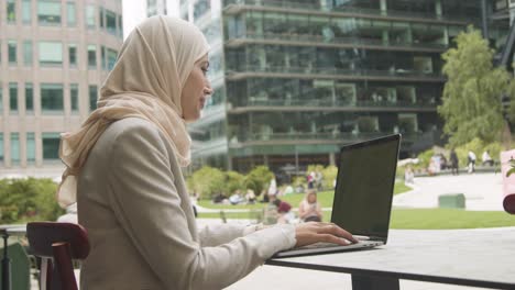 Muslimische-Geschäftsfrau-Sitzt-Draußen-In-Stadtgärten-Und-Arbeitet-Am-Laptop-1