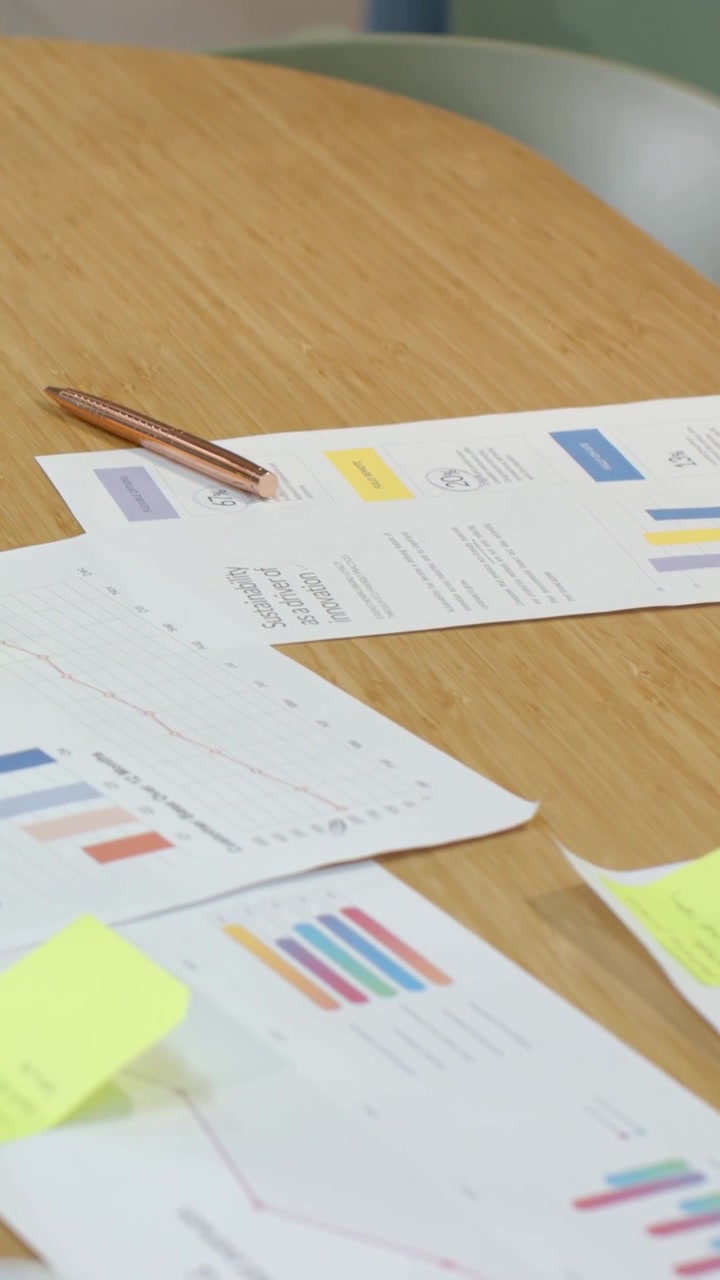 Vertical video: Panning camera showing charts on table in office with pen, sticky notes for review