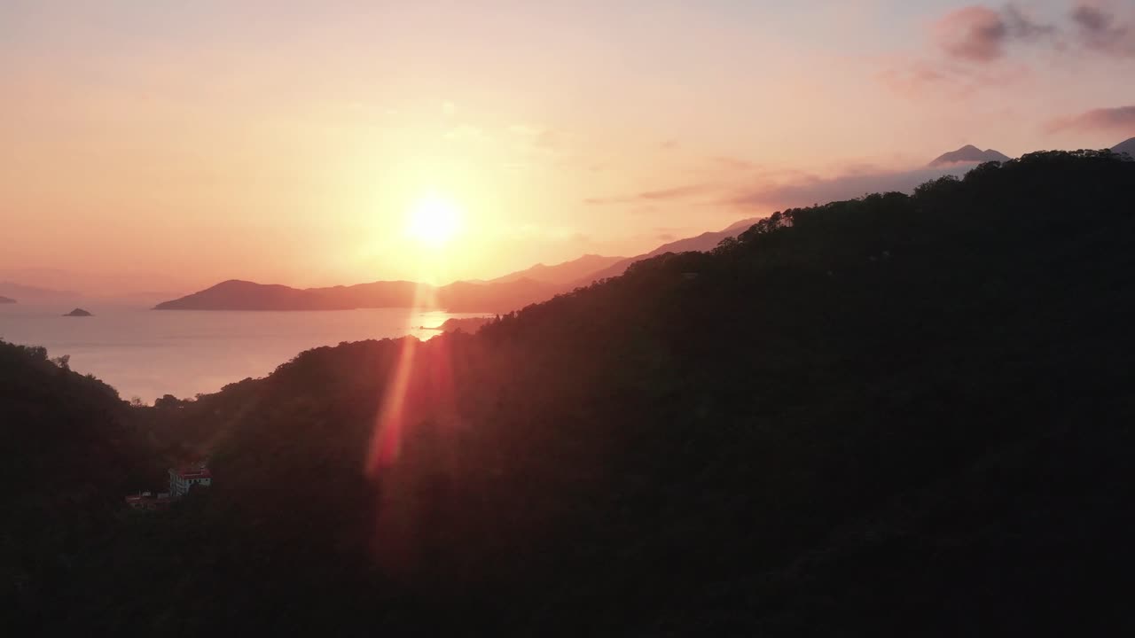 Aerial rising over Pui O bay village, rainforest hills and sea, at sunset with sun beams, Lantau Island, Hong Kong, China