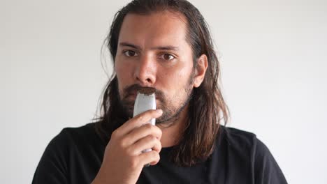 latino man trimming beard and mustache with electric razor, straight razor