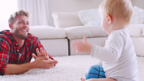 Junger-Vater-Liegt-Auf-Dem-Boden-Und-Klatscht-Mit-Seinem-Kleinen-Sohn-Zu-Hause