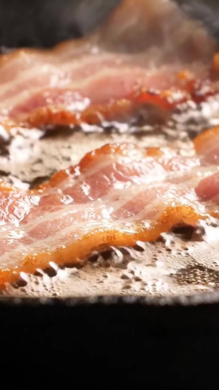 Sprød bacon steger på en varm pande: Sprøde skiver steger i lækkert fedt, hvilket skaber en mundvandsløbende aroma og fristende tekstur for enhver morgenmadselsker