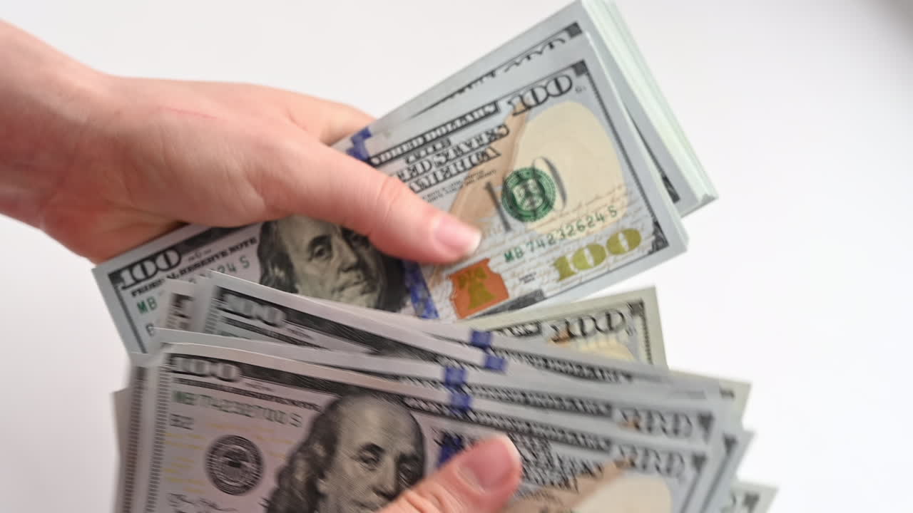 A woman's hands quickly count a stack of one hundred dollar bills against a light background