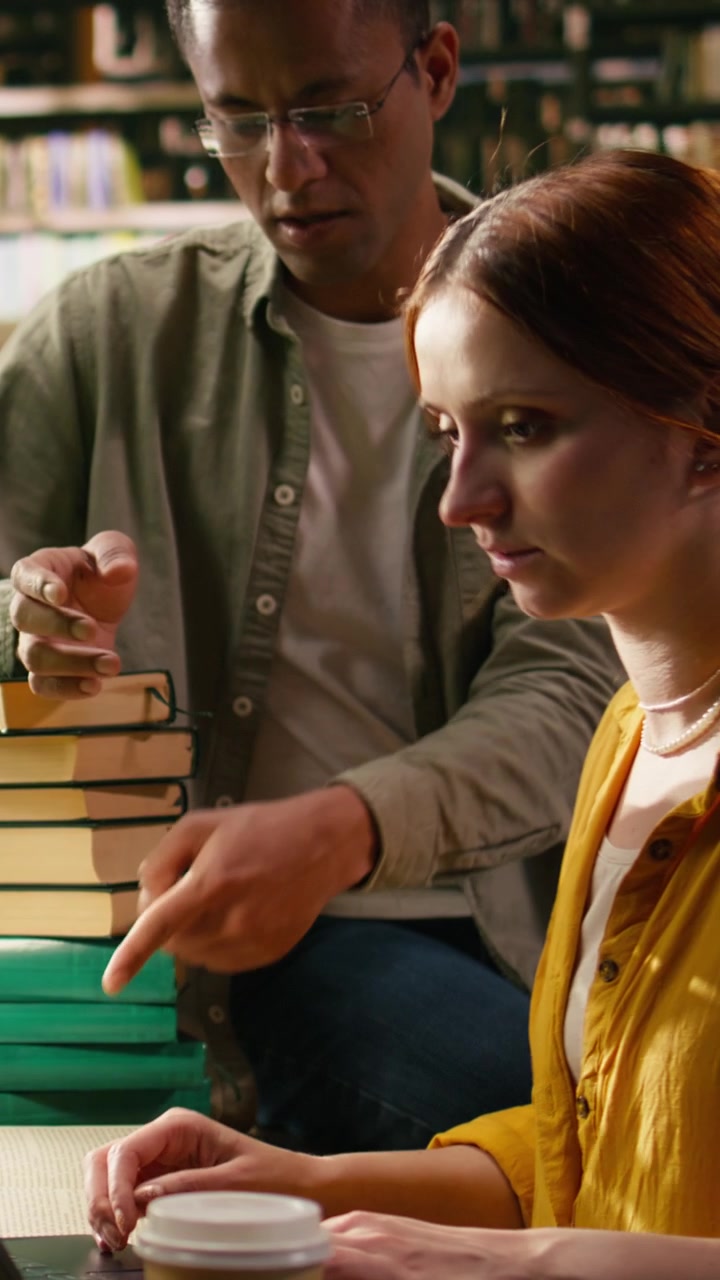 Video verticale: Tutor che assiste una giovane donna che lavora al laptop in una biblioteca universitaria.