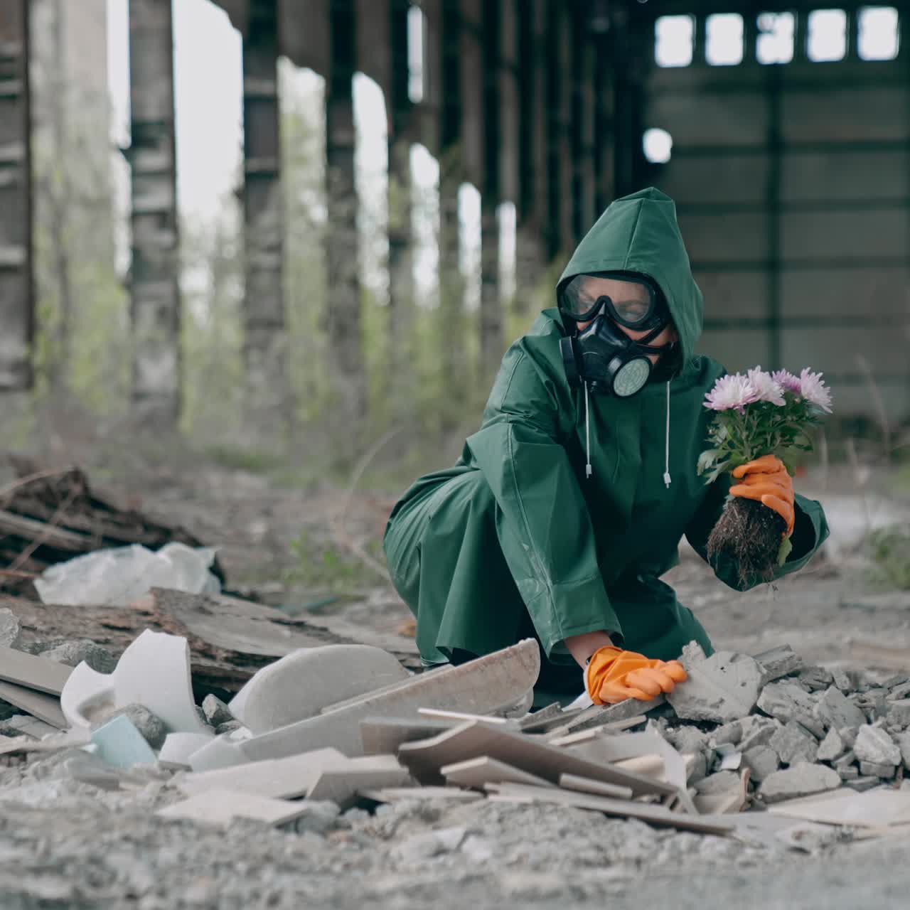 Human trying to save flowers in radioactive zone. Ecologist in safety green suit and gas mask with bunch of flowers inside the ruined building. Chemical attack